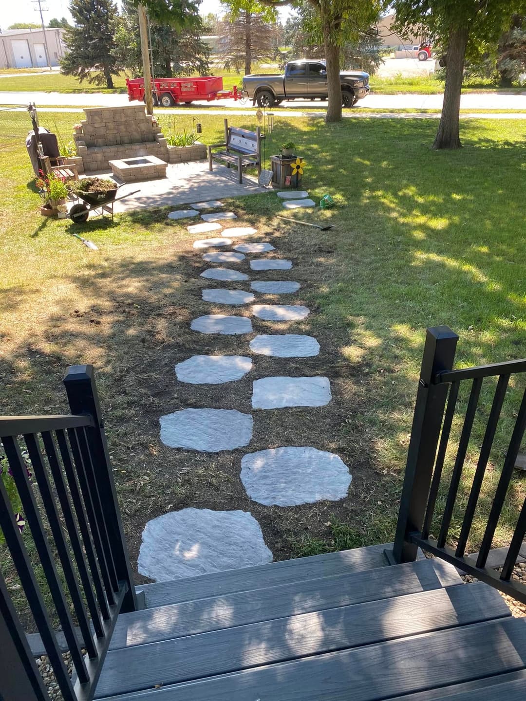 Stone pathway leading through a grassy yard towards a patio area and parked vehicles.