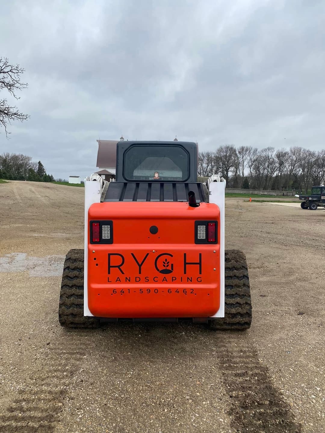 RYCH Landscaping skid steer loader on gravel ground with cloudy sky, showcasing branding.