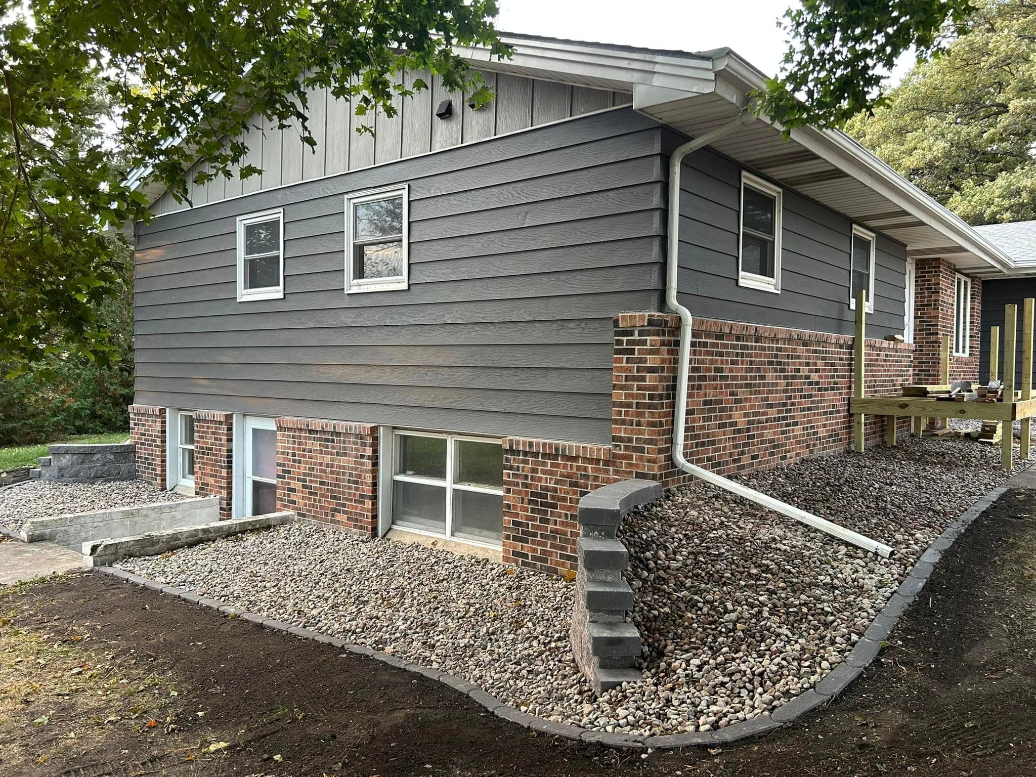 Modern home exterior with gray siding, brick foundation, and landscaped gravel pathway.