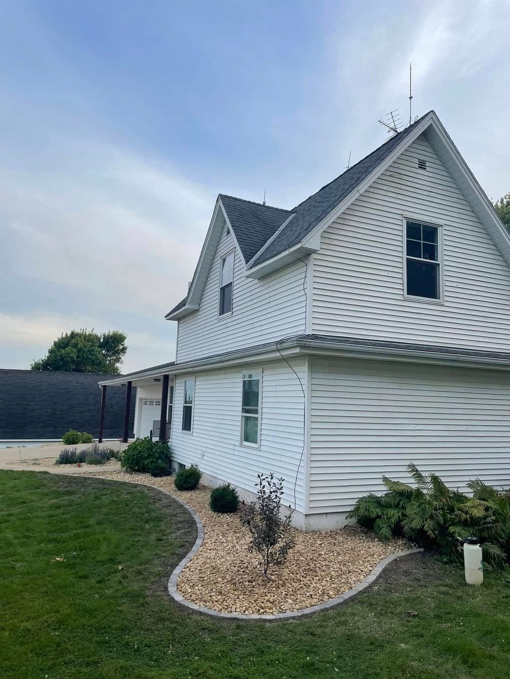 White two-story house with a well-maintained garden and fresh mulch in the foreground.